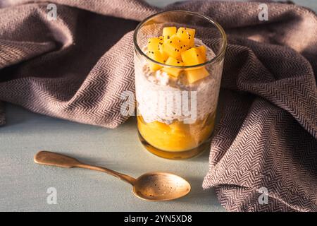 Pudding aux graines de chia, purée de mangue et lait de coco sur la table avec une cuillère et une serviette grise. Concept de petit déjeuner sain, végétalien, desserts crus sans sucre Banque D'Images