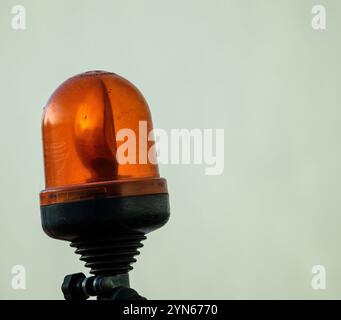 Un feu de signalisation rotatif orange est monté sur une base robuste. La lumière reflète une lueur douce, contrastant avec un fond neutre Uni, créant un Banque D'Images