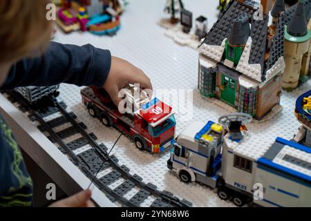 Un enfant joue avec un moteur de pompier jouet. Mains de l'enfant jeu de gros plan dans un constructeur de couleur Lego. Minsk, Biélorussie - 24 novembre 2024 Banque D'Images