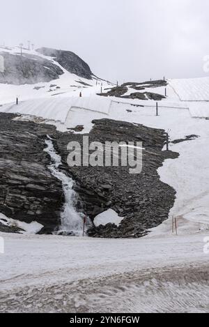 Une grande bâche de neige protégeant la glace du glacier Hintertux dans les Alpes, une cascade d'eau de fonte coule le long de la roche, Autriche, Europe Banque D'Images