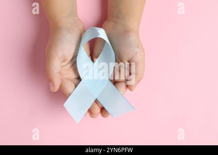 Enfant avec ruban bleu clair sur fond rose, vue de dessus. Sensibilisation au cancer de l'enfant Banque D'Images