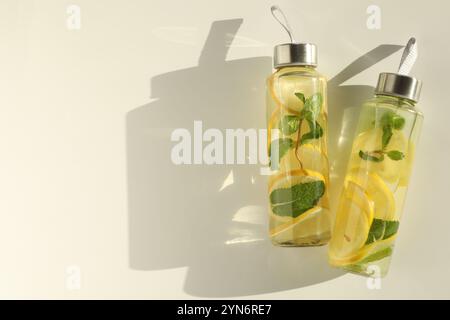 Eau citronnée à la menthe en bouteilles, fruits frais et feuilles sur table blanche, vue de dessus. Espace pour le texte Banque D'Images