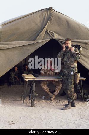 Première Guerre du Golfe : 11 mars 1991 un soldat américain fait un appel téléphonique pendant qu'un soldat britannique du 1st Queen's Own Highlanders garde des prisonniers de guerre irakiens dans une tente de campagne au siège divisionnaire britannique au Koweït. Banque D'Images