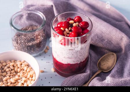 Pudding avec des canneberges, du yaourt, des graines de chia et des pignons de pin sur une table bleue avec une cuillère et une serviette grise. Concept de petit déjeuner délicieux et sain, ve Banque D'Images