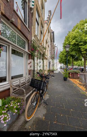 Une charmante vue sur la rue avec un vélo garé près d'un banc en bois, entouré de fleurs colorées. De grands bâtiments historiques bordent le sentier sous un dr. Banque D'Images