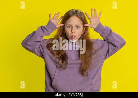 Portrait de jeune fille d'école rousse drôle montrant la langue faire des visages à la caméra, tromper autour, plaisanter, aping avec un visage stupide, taquiner, intimider l'abus. Enfant femelle de preteen sur fond jaune Banque D'Images