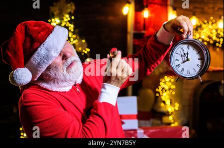 Père Noël regardant à travers une loupe à l'horloge de Noël. C'est l'heure de Noël. Le Père Noël regarde à travers la loupe au réveil du nouvel an qui Banque D'Images