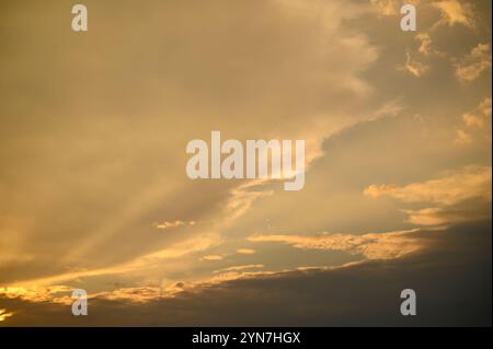 Une lumière dorée douce projette une lueur chaude sur les nuages alors que le jour passe à la nuit, créant une atmosphère paisible. Banque D'Images