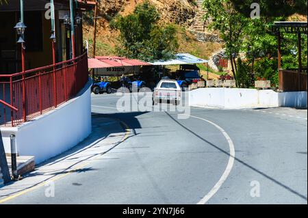 Gaziveren Chypre -23.11.2024 Une voiture classique navigue sur une route sinueuse dans un charmant village, entouré d'une végétation luxuriante et d'une lumière chaude du soleil. Banque D'Images