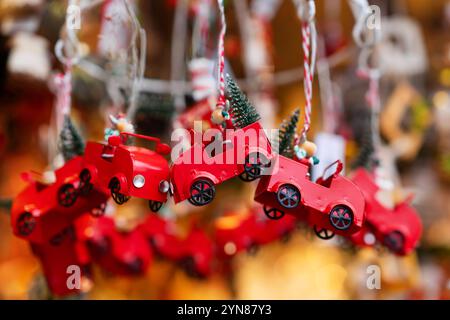 Les voitures jouets en métal rouge ornées de petits arbres de Noël verts sont suspendues comme ornements festifs. Ces décorations capturent la sensation de vacances nostalgique, perfec Banque D'Images