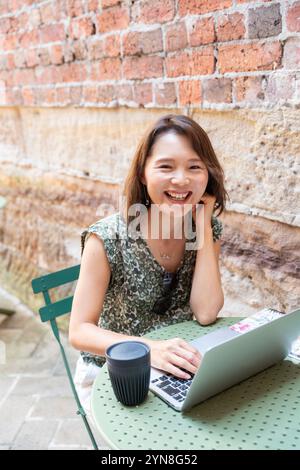 Femme souriante avec ordinateur ouvert dans le café Banque D'Images