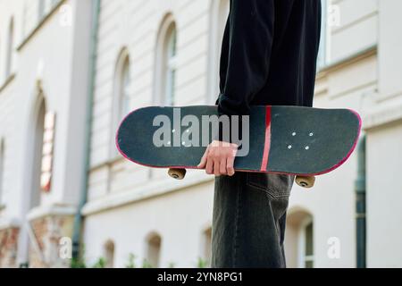 Skateboarder dans un Jean baggy tenant un skateboard rayé marchant dans la rue de la ville. Adolescent fait du skateboard. Concept de sous-culture de la jeunesse Banque D'Images