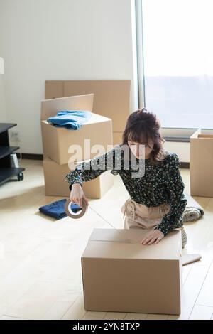 Femme dans la vingtaine mettant du ruban adhésif sur du carton Banque D'Images