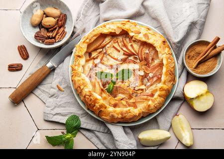 Galette de pommes fraîchement cuite décorée de flocons d'amandes, de feuilles de menthe, de cannelle et de noix de pécan, servie sur une assiette en céramique Banque D'Images