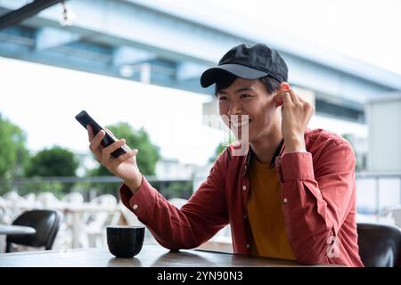 Homme dans la vingtaine tenant et souriant à un smartphone dans un café Banque D'Images