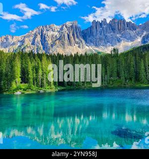 Un lac alpin tranquille affiche de superbes eaux turquoises entourées d'arbres luxuriants à feuilles persistantes, reflétant les imposantes montagnes baignées de soleil. Karersee ou Lago Di Carezza Dolomites Italie Banque D'Images