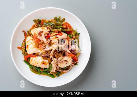 Tumis Cumi tauco ou Squid Stir Fried épicé avec tauco servi sur assiette blanche et isolé sur fond gris. Tauco est une pâte faite à partir de fer conservé Banque D'Images