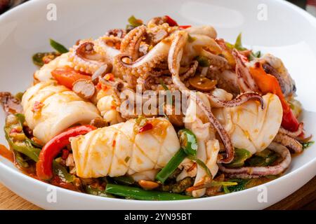 Tumis Cumi tauco ou Squid Stir Fried épicé avec tauco servi sur assiette blanche et isolé sur fond gris. Tauco est une pâte faite à partir de fer conservé Banque D'Images