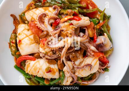 Tumis Cumi tauco ou Squid Stir Fried épicé avec tauco servi sur assiette blanche et isolé sur fond gris. Tauco est une pâte faite à partir de fer conservé Banque D'Images