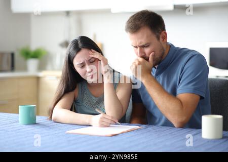 Triste couple interracial ou colocataires lisant contrat dans la cuisine à la maison Banque D'Images