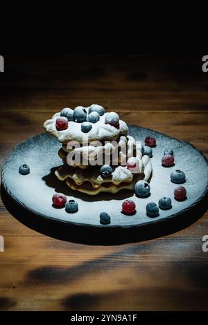 Gaufres belges aux canneberges et aux bleuets saupoudrées de sucre en poudre sur une table en bois sur une assiette noire. Photo de haute qualité Banque D'Images