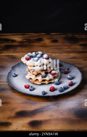 Gaufres belges aux canneberges et aux bleuets saupoudrées de sucre en poudre sur une table en bois sur une assiette noire. Photo de haute qualité Banque D'Images