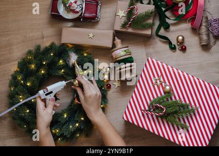 Vue de dessus d'une femme utilisant un pistolet à colle pour coller des jouets à une couronne de Noël. Holliday Mood Banque D'Images