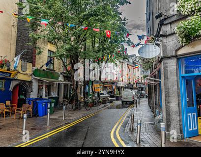 Une rue européenne animée bordée de boutiques et de cafés, décorée de drapeaux colorés. Les gens et les véhicules remplissent la route pavée animée, highlighti Banque D'Images