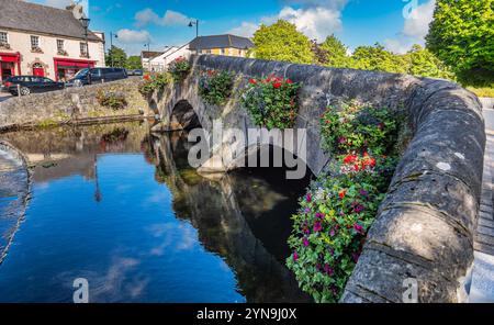 Une scène pittoresque avec un charmant pont de pierre orné de fleurs sur une rivière sereine, situé dans un village européen pittoresque avec archite historique Banque D'Images