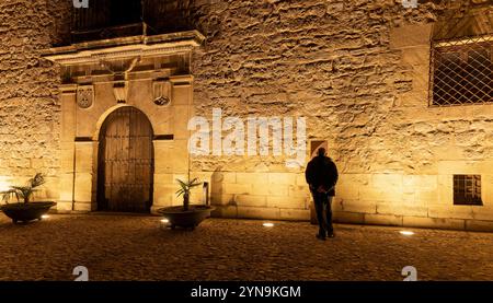 Un homme se tient devant un bâtiment avec une grande porte. Le bâtiment est vieux et a un extérieur en pierre. L'homme porte une veste noire et il est looki Banque D'Images