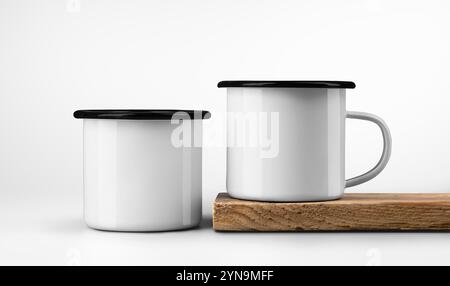 Modèle de deux tasses en métal blanc avec jante noire, sur le bord de la vieille planche de bois, tasses en fer sur bois texturé, isolé sur fond. Mug en émail maquette sur t Banque D'Images