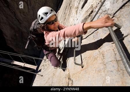 Une jeune femme clipsant une échelle encastrée dans le rocher tout en pratiquant le sport de la via Ferrata à Val D'isère, France. Banque D'Images