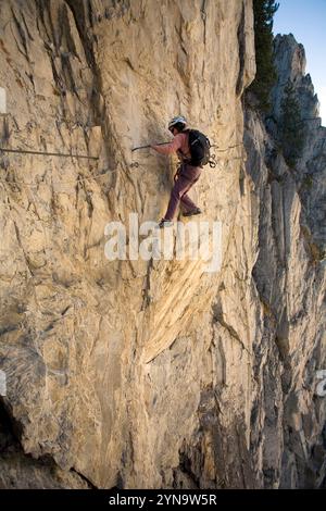 Une jeune femme traverse une falaise tout en pratiquant le sport de la via Ferrata à Val D'isère, Savoie, France. Banque D'Images