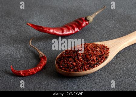 Flocons de poivre. Piments rouges dans une cuillère en bois sur fond noir. Piments secs Banque D'Images