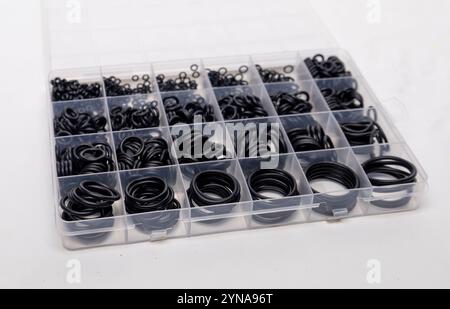 Différentes tailles de joints toriques en caoutchouc noir sont soigneusement disposés dans une boîte d'organisateur en plastique transparent, mettant en valeur leur variété pour diverses applications Banque D'Images