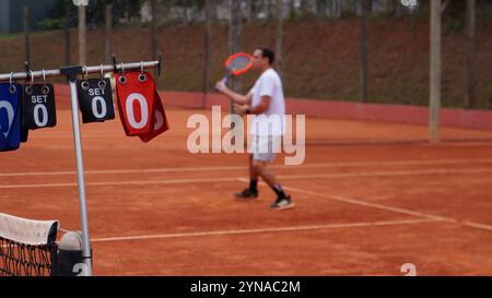 Tableau d'affichage sur un court de tennis avec un joueur en arrière-plan hors de focus Banque D'Images