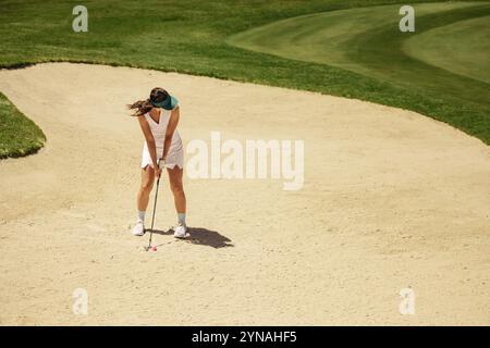 Golfeuse dans le bunker de sable visant et se préparant à prendre un coup de feu. Elle maintient une position concentrée comme elle se concentre sur frapper la balle de golf. Banque D'Images