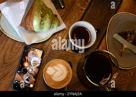 Un cadre de café délicieux avec un latte avec de l'art, une théière de café, un croissant au beurre et un cheesecake. Parfaitement confortable Banque D'Images