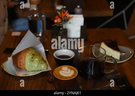 Un cadre de café délicieux avec un latte avec de l'art, une théière de café, un croissant au beurre et un cheesecake. Parfaitement confortable Banque D'Images