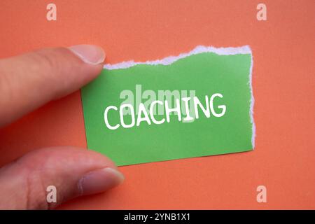 Message de coaching écrit sur un papier déchiré vert déchiré sur fond orange. Symbole de coaching conceptuel. Copier l'espace. Banque D'Images