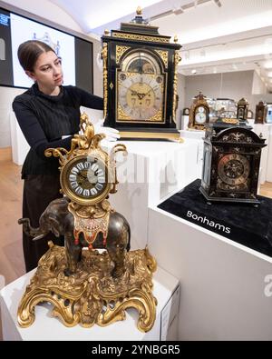 Londres, Royaume-Uni. 25 novembre 2024. Un membre du personnel avec (en haut) Une belle horloge de table musicale ébonisée à 12 airs montée en laiton du milieu du XVIIIe siècle, par James Upjohn, estime £7 000 - £10,000, lors d'un aperçu des œuvres dans les ventes aux enchères de la saison Winter Classics à Bonhams New Bond Street. Des lots seront mis en vente lors de la vente Fine Clocks, le 27 novembre, dans les galeries Bonhams de New Bond Street. Credit : Stephen Chung / Alamy Live News Banque D'Images