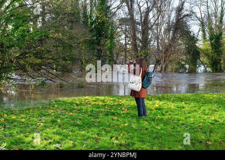 Chippenham, Wiltshire, Royaume-Uni, 25 novembre 2024. Une femme est photographiée à Monkton Park en train de prendre une photo du Rver Avon inondé après que la rivière a éclaté ses rives dans le centre-ville. Crédit : Lynchpics/Alamy Live News Banque D'Images