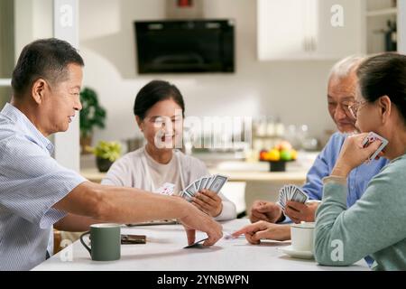 groupe de personnes âgées asiatiques heureuses deux couples se réunissant à la maison à jouer aux cartes ensemble Banque D'Images