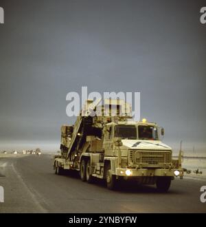 Première Guerre du Golfe : 12 mars 1991 dans le nord du Koweït, une colonne de camions de l'armée britannique se dirige vers le sud sous des nuages sombres de fumée provenant des puits de pétrole brûlés. Les camions sortent du Koweït, se dirigeant vers un port en Arabie saoudite. Le véhicule de tête est un transporteur de chars Scammell commander (TK/TPTR) et il transporte deux FV510 Warrior IFV (Infantry Fighting Vehicles). Banque D'Images