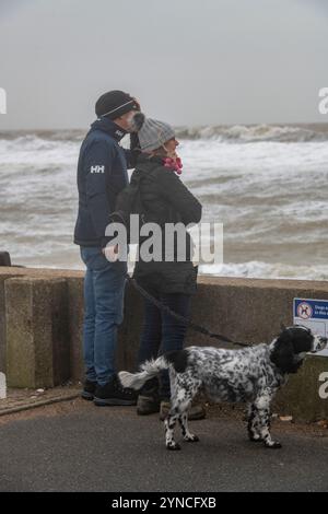 homme et femme couple avec leur chien debout au bord de la mer regardant une tempête et les vagues brisées, les promeneurs de chiens regardant les mers orageuses île de wight. Banque D'Images