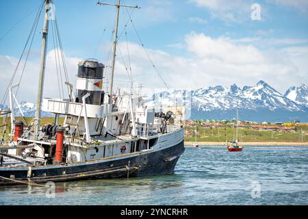 USHUAIA, Argentine — le Saint Christopher (anciennement HMS Justice) se trouve échouée dans le port d'Ushuaia sur fond de montagnes enneigées. Le remorqueur de sauvetage de la seconde Guerre mondiale a été délibérément échoué en 1957 après avoir éprouvé des problèmes de moteur lors des opérations de sauvetage. Le navire sert maintenant de monument à l'histoire maritime de la région du canal Beagle. Banque D'Images