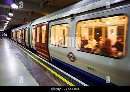 LONDRES, Angleterre — Un train de métro londonien part d'un quai de gare, démontrant le fonctionnement du système de métro historique de la ville. Le Banque D'Images