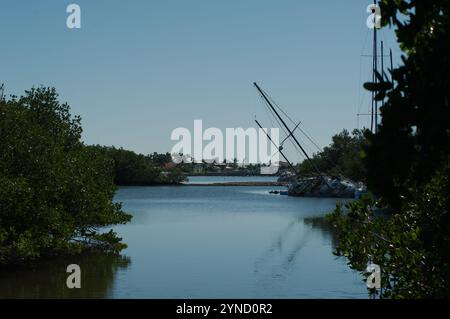 Large vue S courbe sur l'eau de Blue Bay encadrée par des mangroves des deux côtés. Deux voiliers échoués endommagés dans des arbres verts avec un quai à l'arrière vers la baie. Banque D'Images