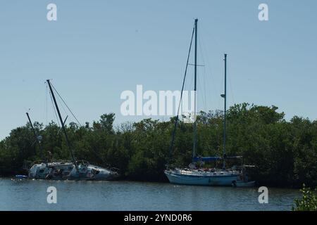 Large vue S courbe sur l'eau de Blue Bay encadrée par des mangroves des deux côtés. Deux voiliers échoués endommagés dans des arbres verts avec un quai à l'arrière vers la baie. Banque D'Images