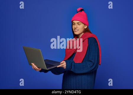 Jeune homme enthousiaste avec de longs cheveux roux s'engage avec son ordinateur portable tout en portant une tenue confortable. Banque D'Images